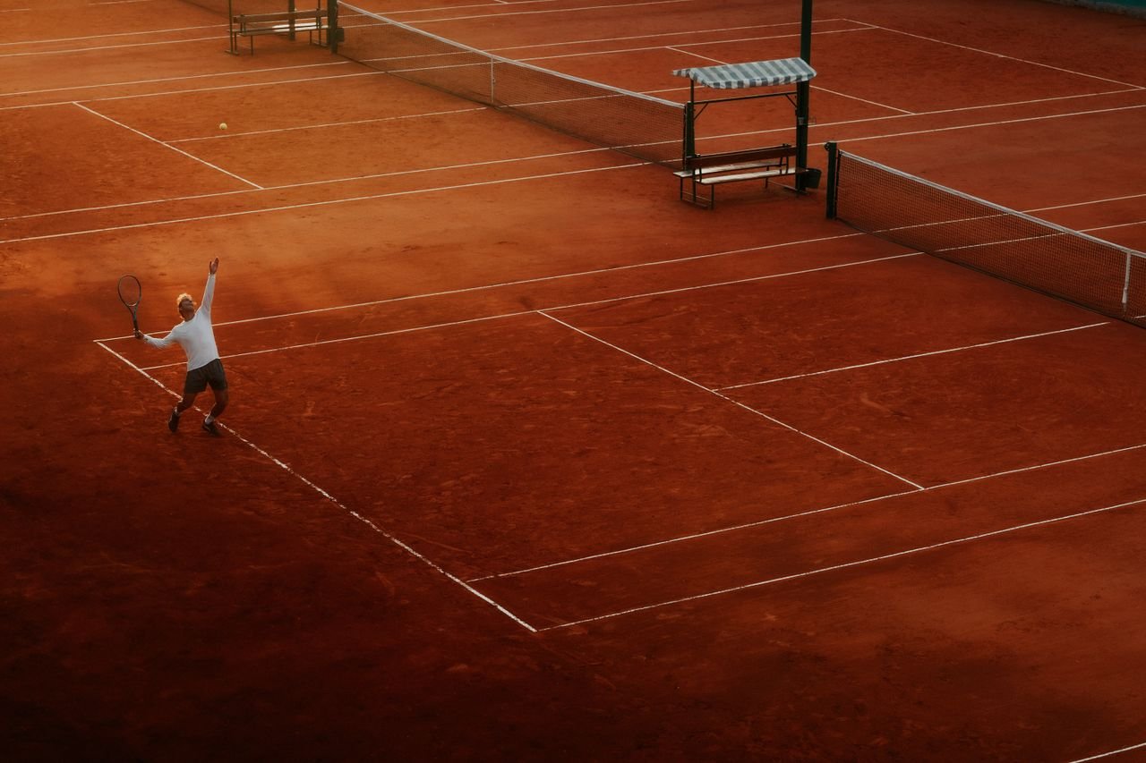 Services A player serves on a clay tennis court, highlighting the beauty and intensity of the sport at sunset.